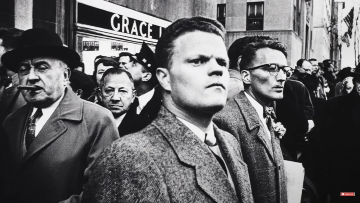 Black and white photograph of men in suits and hats in a crowded street scene with signage visible in background.