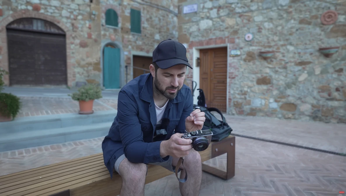 Photographer holding a mirrorless camera while seated outdoors in a historic stone courtyard.