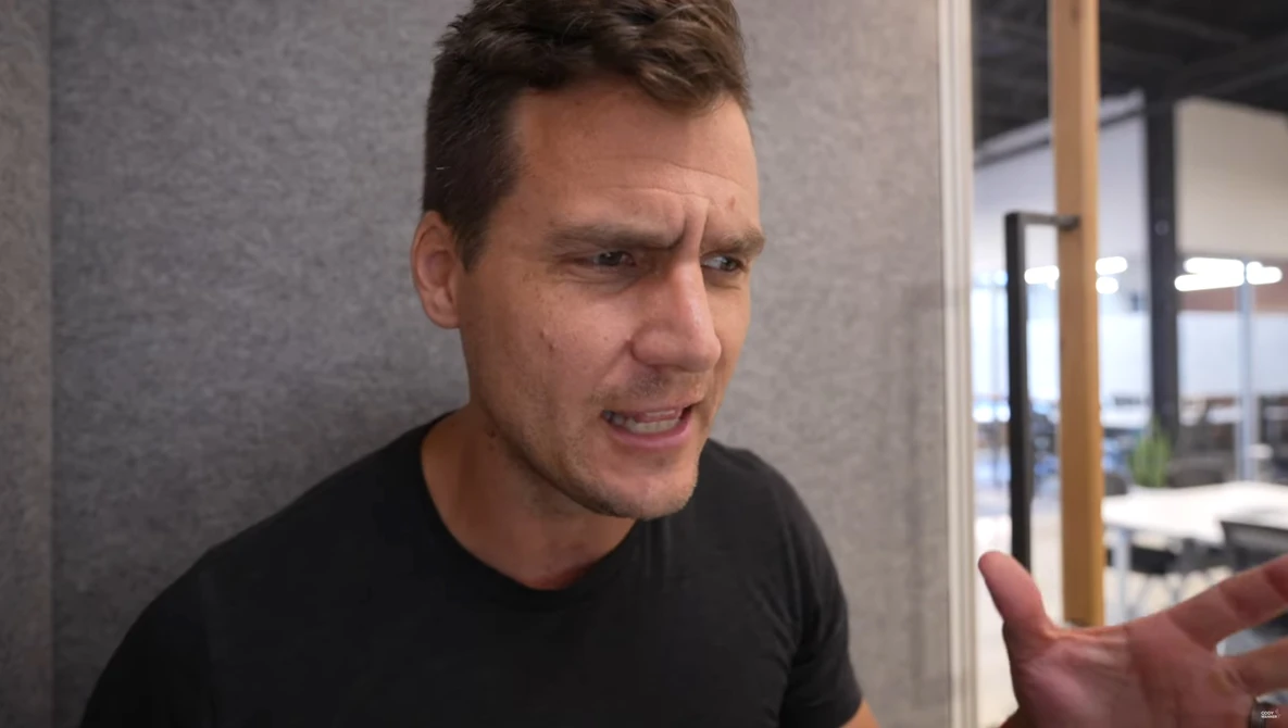 Man in black shirt gesturing while speaking in a modern office setting.