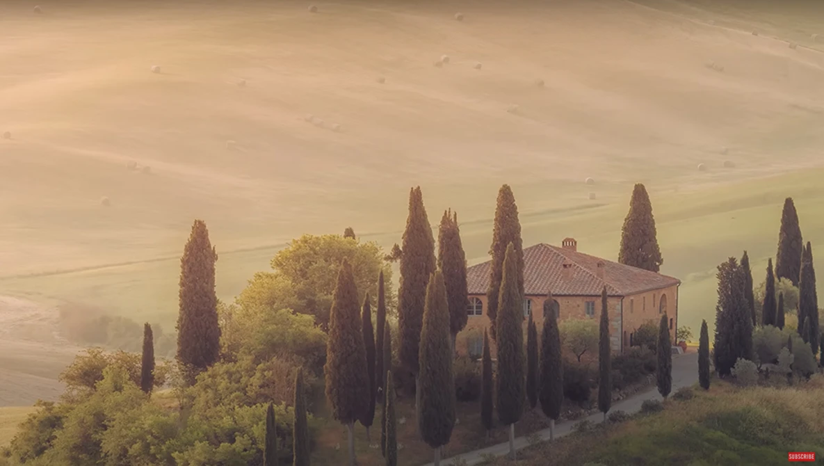 Tuscan villa surrounded by cypress trees in rolling hills at golden hour.