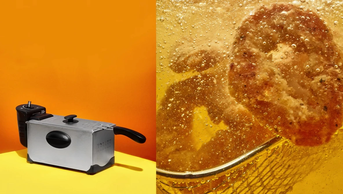 Deep fryer with stainless steel body and black handles on yellow surface against orange background.