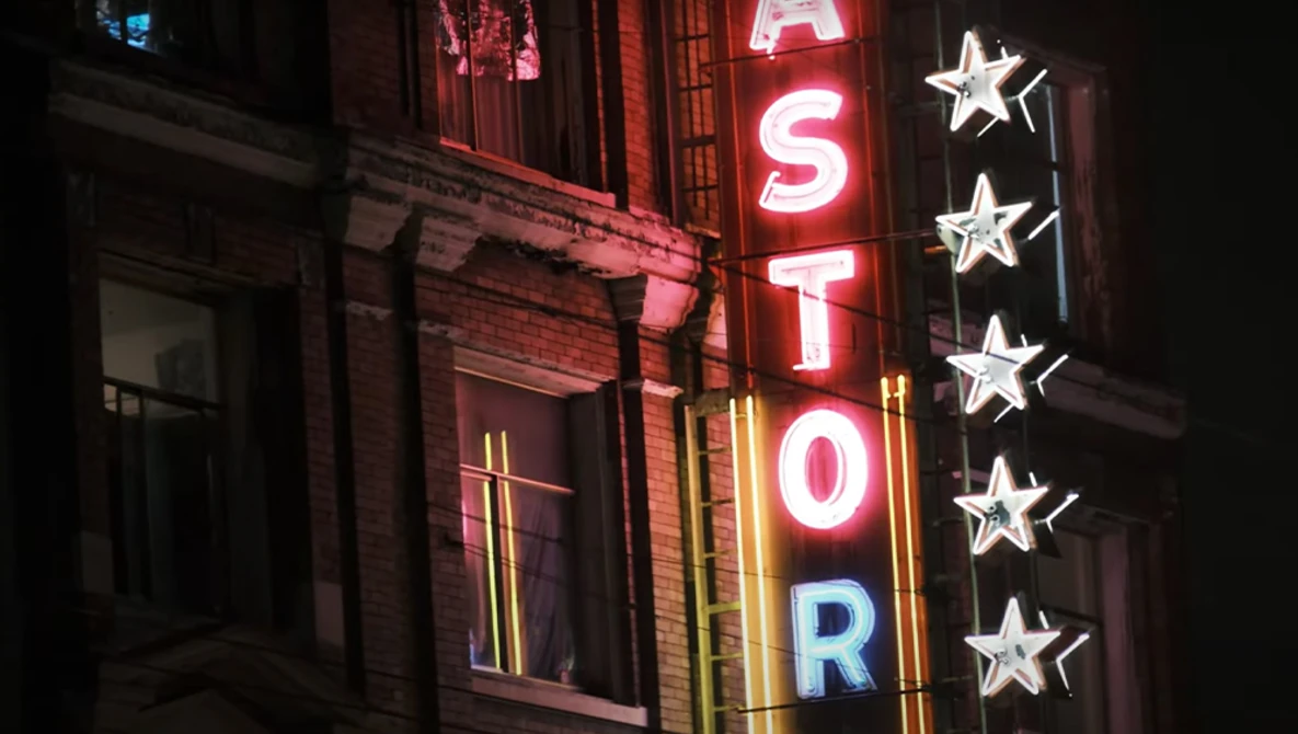 Neon sign reading "ASTOR" with illuminated stars on a brick building facade at night.