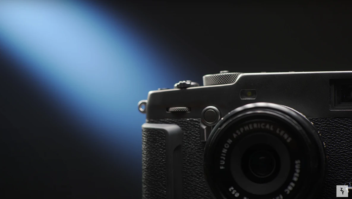 Compact rangefinder camera with textured black body positioned against a dark background with blue directional lighting.