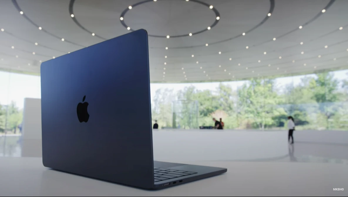 Dark blue MacBook laptop displayed at an angle in a minimalist interior space with curved ceiling and recessed lighting.