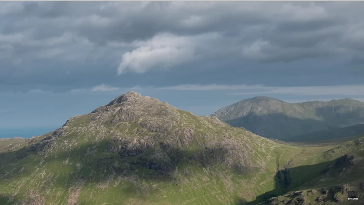 Rocky mountain peak with green slopes under dramatic cloudy sky and distant coastline.