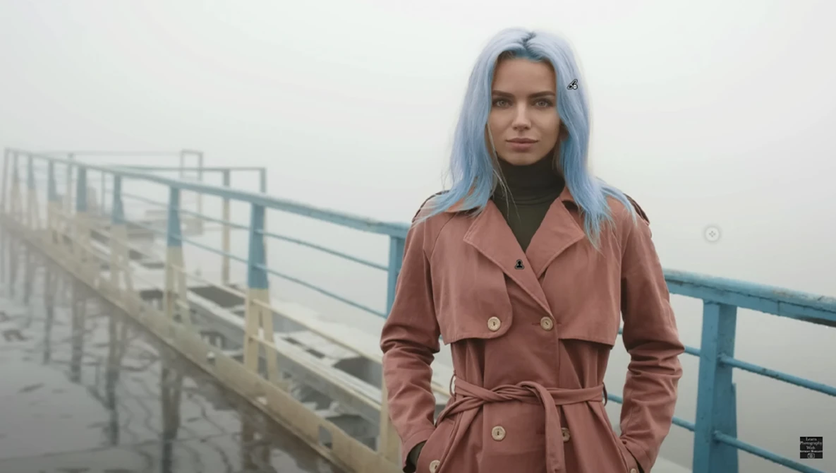 Woman with blue hair wearing a mauve trench coat stands on a misty bridge.
