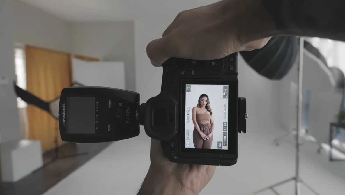 Photographer's hand holding a camera displaying a portrait of a woman on its rear LCD screen during a studio shoot.