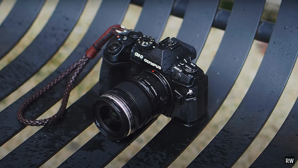 Black mirrorless camera with attached lens on striped blue and white background with red camera strap.