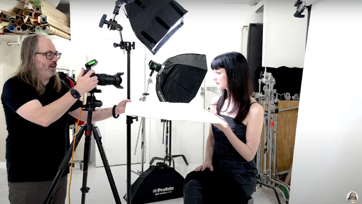 Cinematographer operating a camera on tripod while filming a subject in a studio with professional lighting setup.