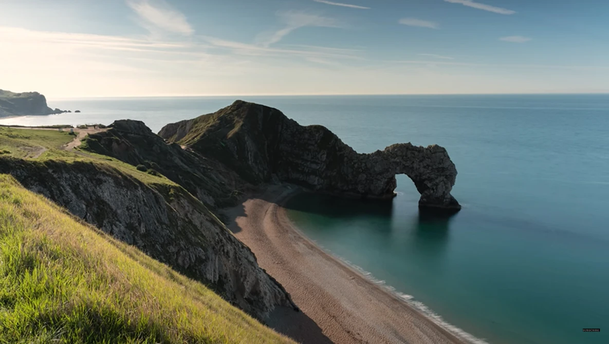 Rocky coastal headland with natural stone arch framing a curved sandy beach and turquoise sea.
