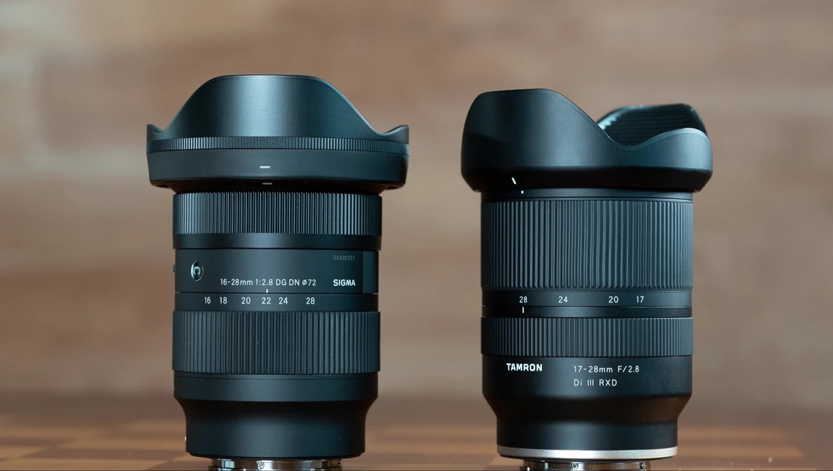Two wide-angle zoom lenses with lens hoods displayed side by side against a blurred background.