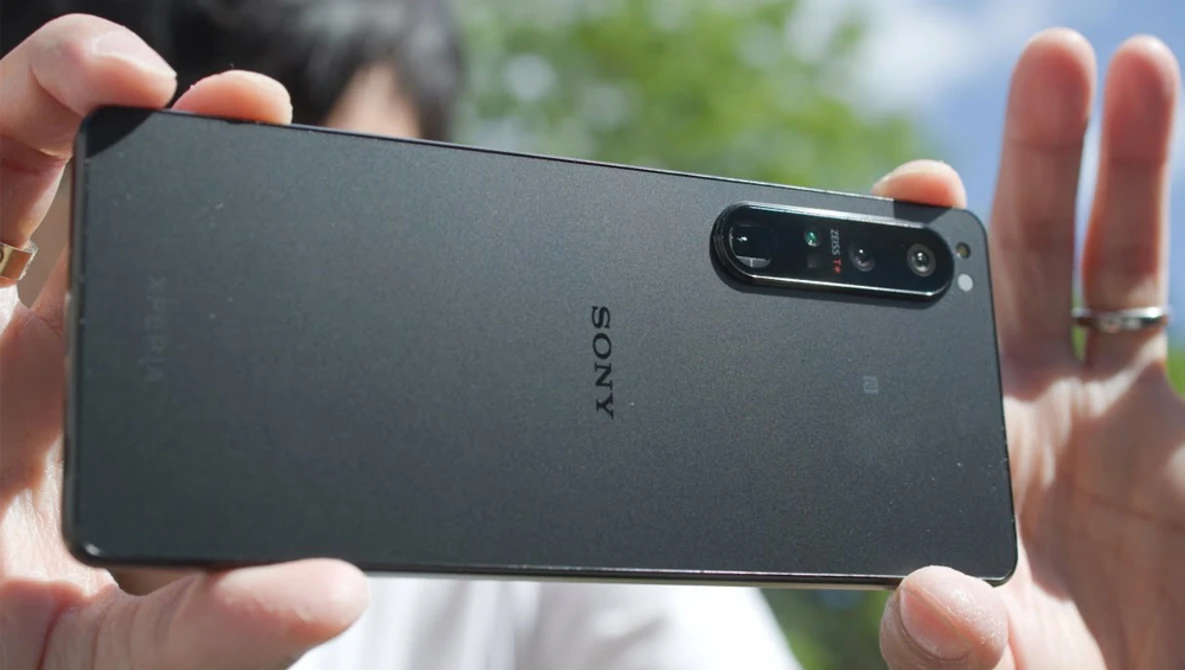 Sony smartphone held in hands outdoors, displaying rear camera module with multiple lenses against blurred green background.