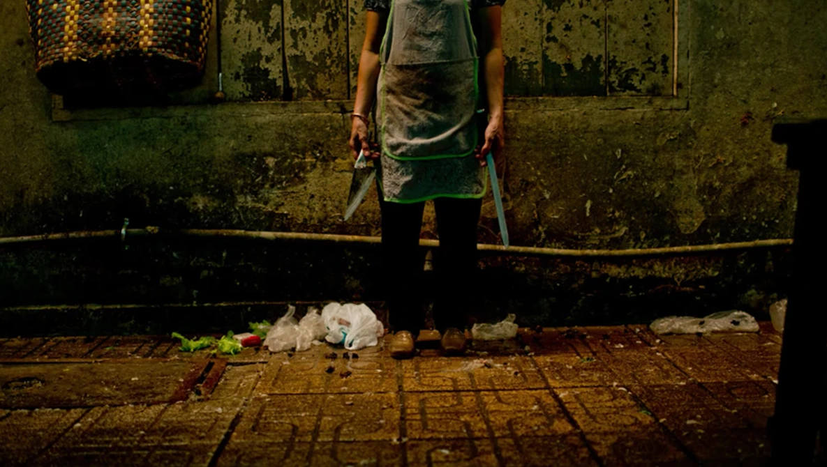 Person in apron standing over fish on tiled floor against weathered green wall.