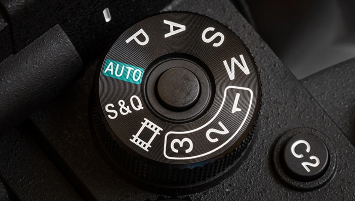 Close-up of a camera mode dial showing AUTO, P, S, A, M, and other exposure modes with manual focus settings.