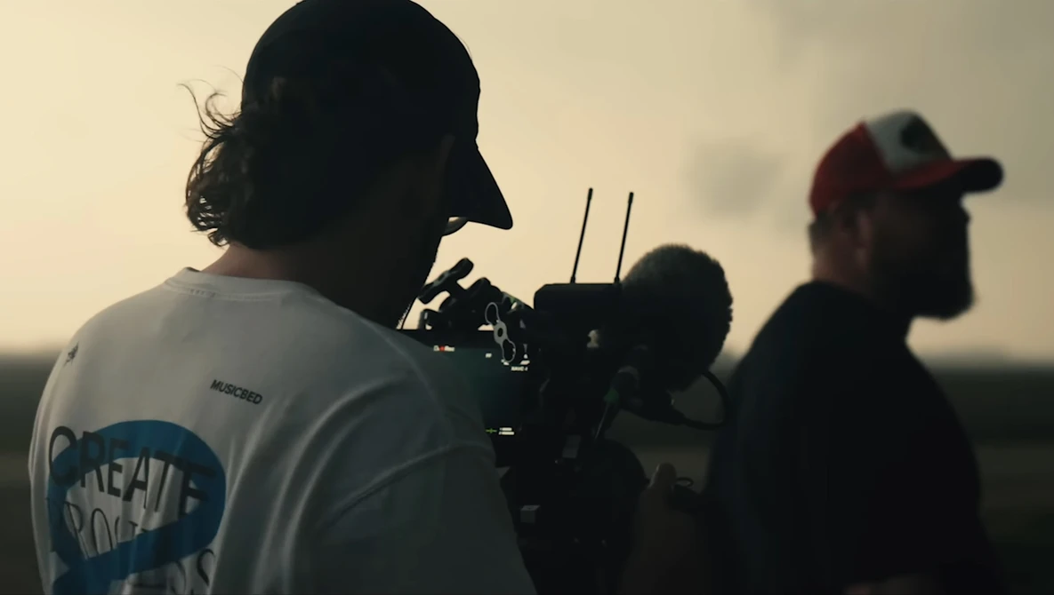 Cinematographer operating a camera rig during golden hour outdoor shoot with crew members visible in background.