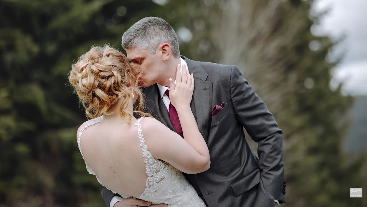 Bride and groom kissing outdoors, with bride wearing beaded backless gown and groom in charcoal suit.