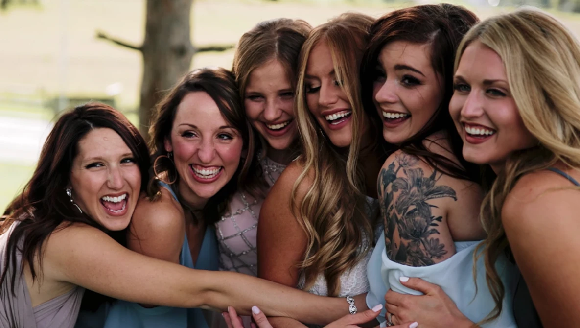 Six women smiling and posing together outdoors in natural daylight.