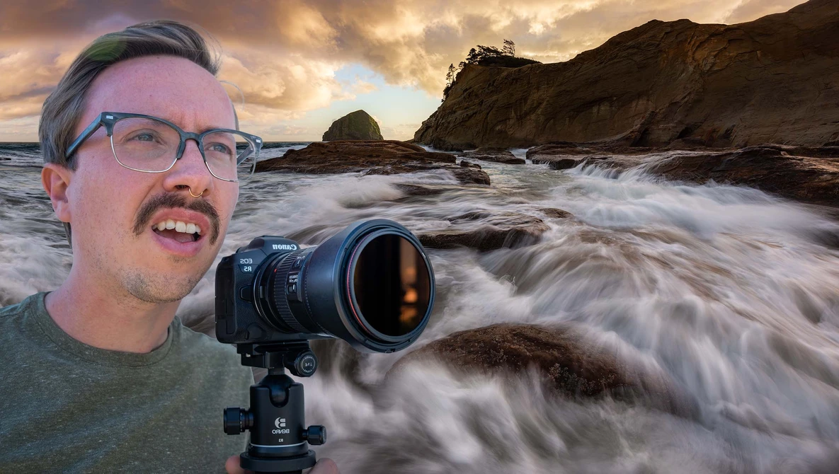 Photographer with camera on tripod at rocky coastline with dramatic waves and sunset sky.
