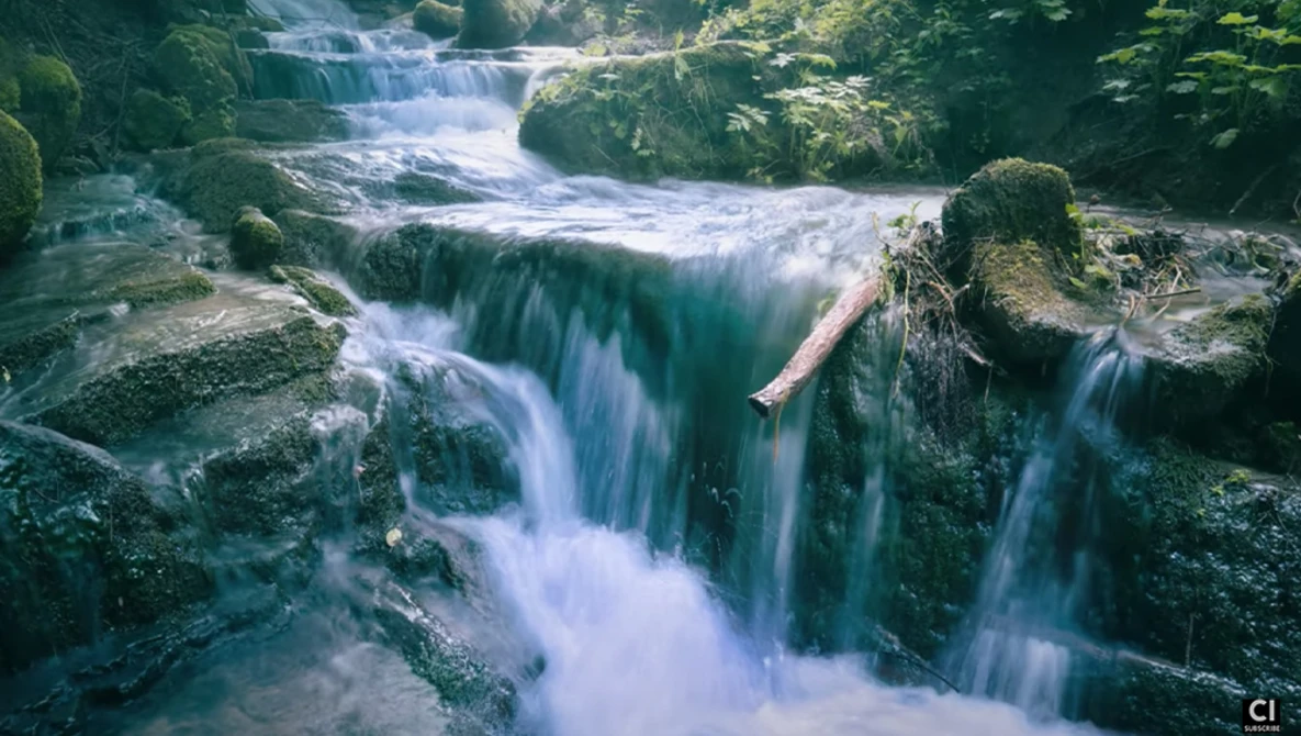 Cascading waterfall flowing over moss-covered rocks through a forested stream.