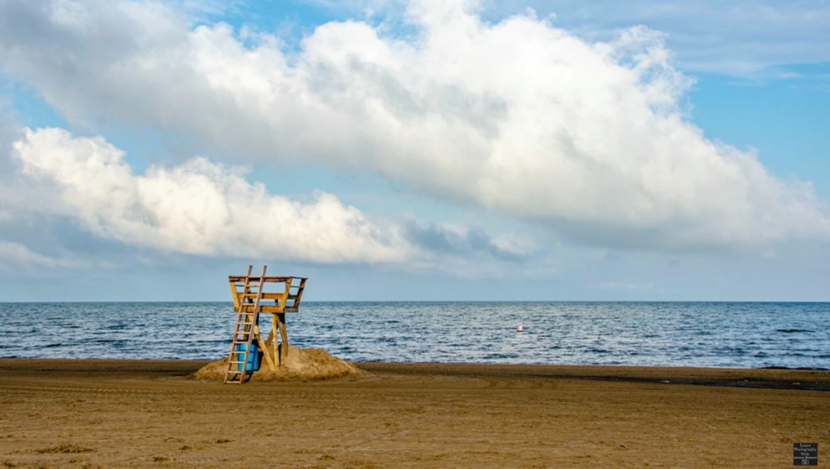 Abandoned yellow lifeguard tower standing alone on an empty beach under a blue sky with white clouds.