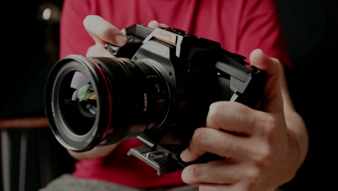 Photographer in pink shirt holding a vintage rangefinder camera with wide-angle lens and flash attachment.