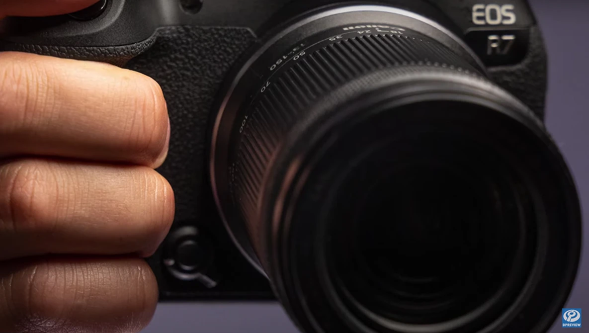 Photographer's hand holding Canon EOS mirrorless camera with attached lens in close-up view.