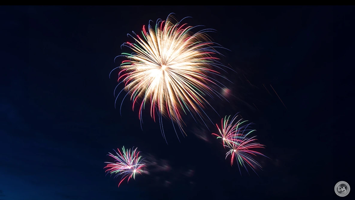 Fireworks bursting against a dark night sky, with a large bright burst in the upper center and smaller explosions below.