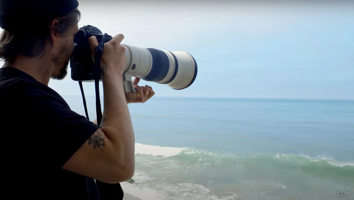 Photographer holding telephoto lens while shooting coastal ocean and beach landscape.