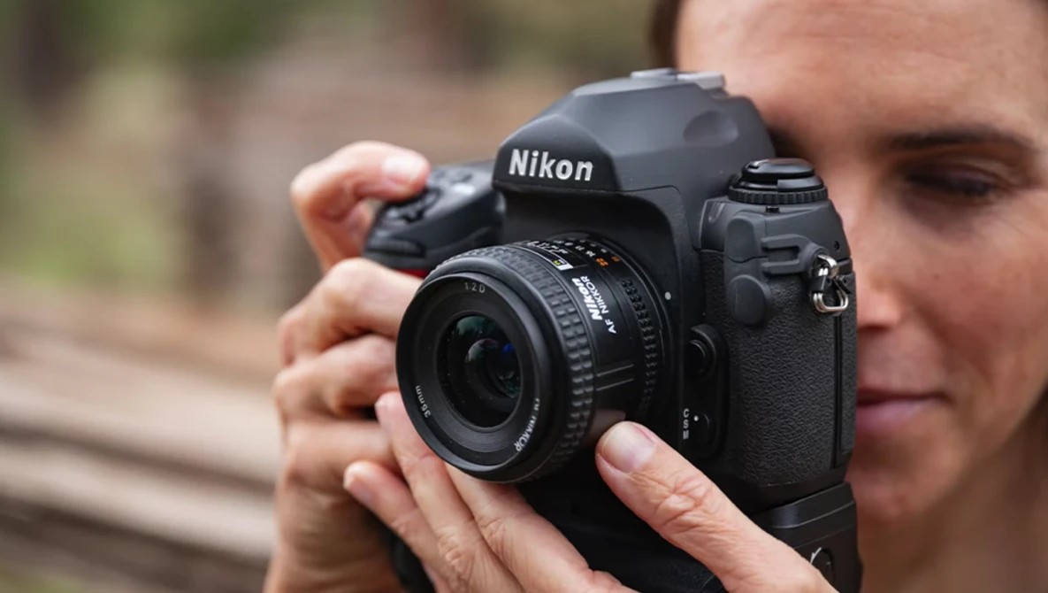 Photographer holding a Nikon DSLR camera with attached lens, demonstrating proper grip and positioning.