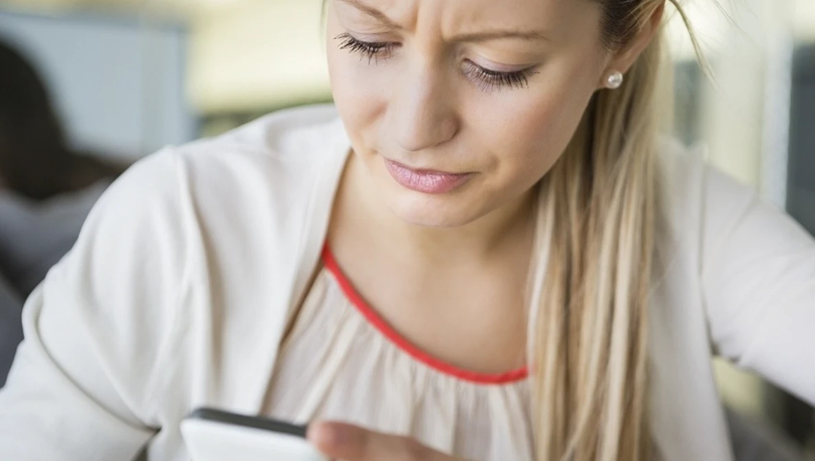 Woman in white shirt with red neckline looking down at smartphone in her hands.