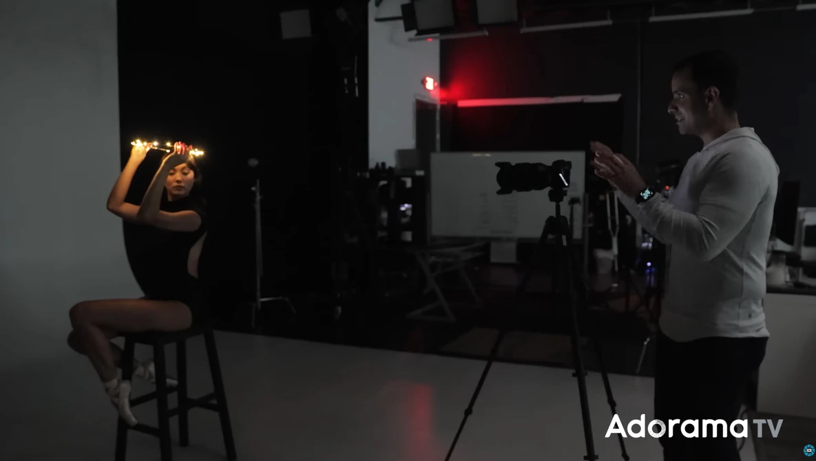 Photographer shooting a portrait of a seated subject in a studio with professional lighting setup.