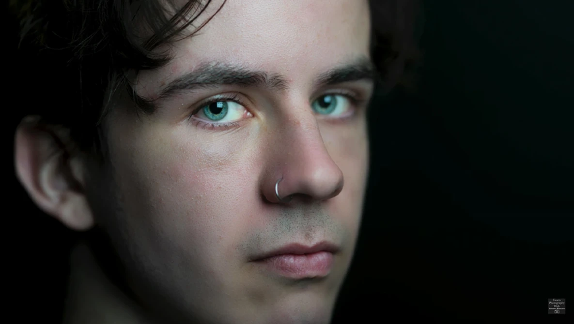 Close-up portrait of a man with striking turquoise eyes against a dark background.