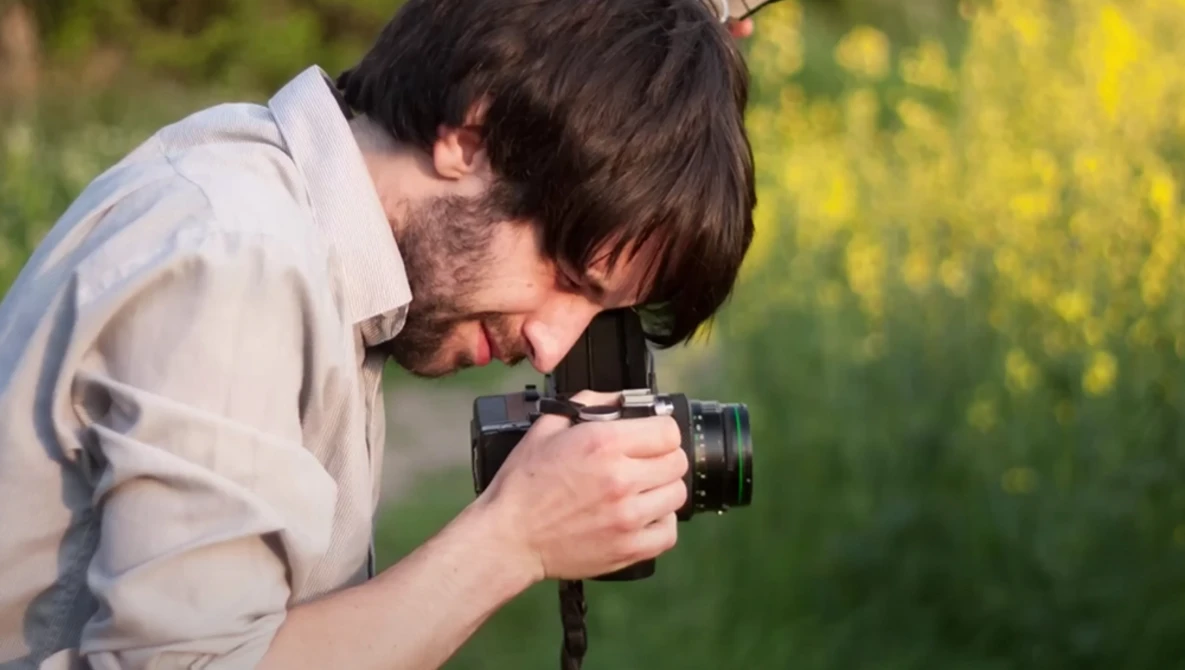 Photographer holding a DSLR camera with a telephoto lens, focused on composing a shot outdoors.