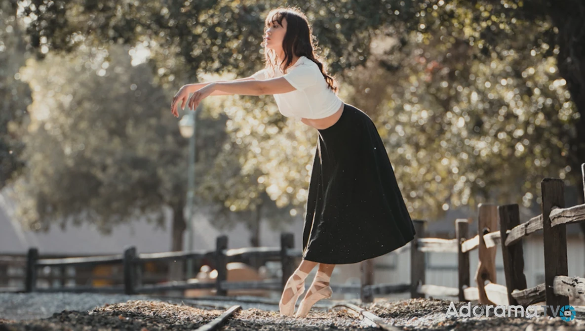 Ballet dancer in pointe shoes performing an arabesque outdoors under golden tree foliage.