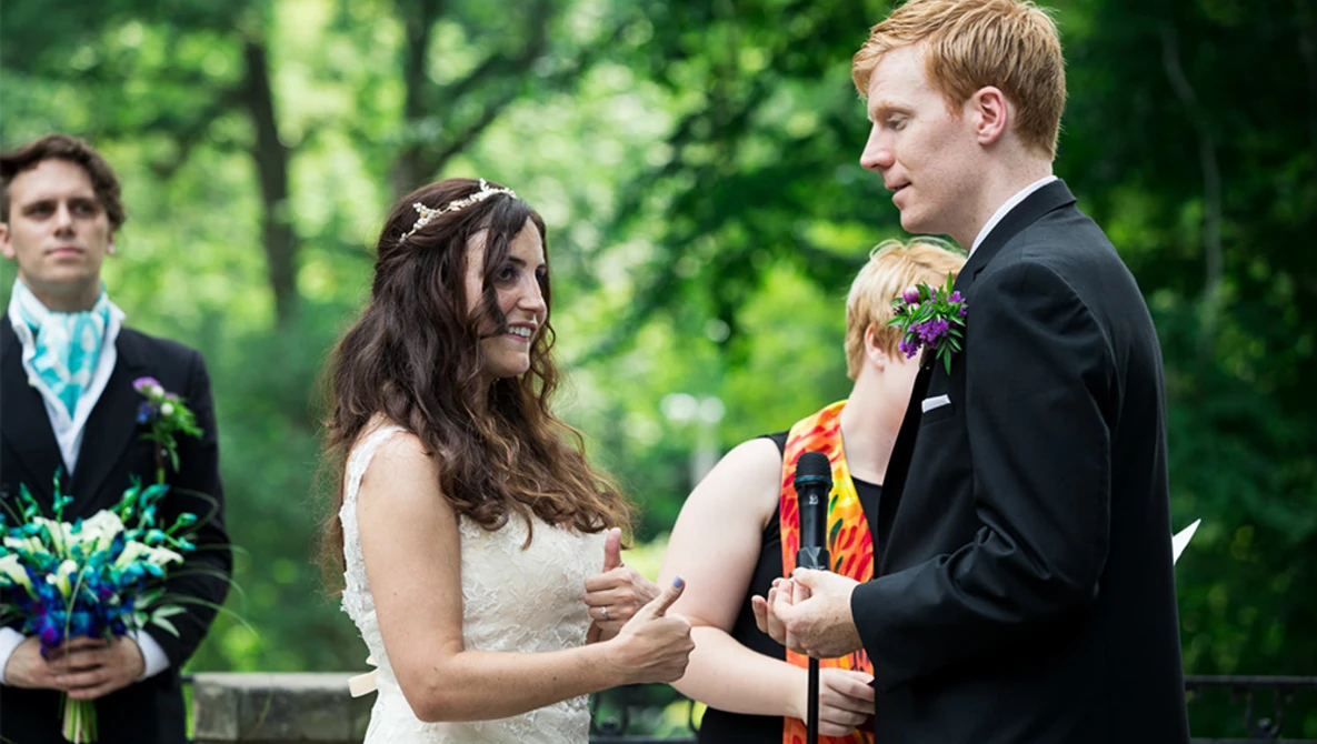 Bride and groom exchange vows during outdoor wedding ceremony with officiant and groomsman present.