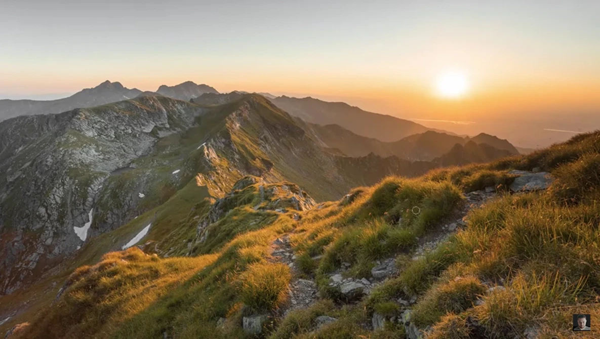 Alpine mountain ridge at golden hour with layered peaks receding into hazy distance.