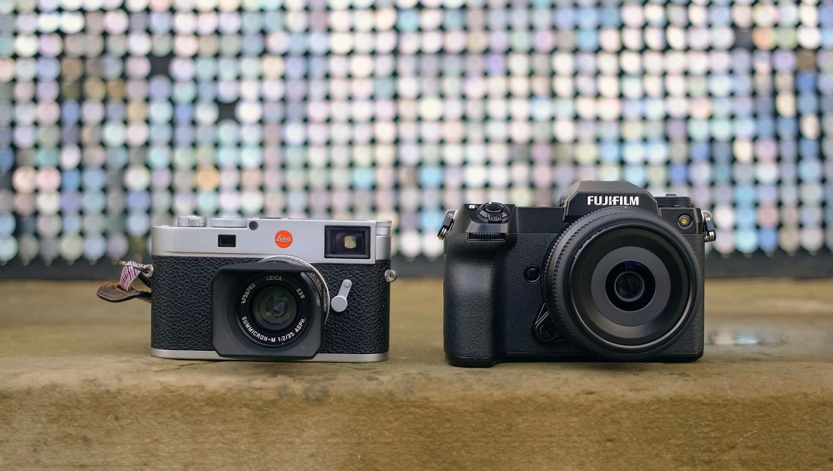 A rangefinder film camera and a mirrorless digital camera displayed side by side on a wooden surface.