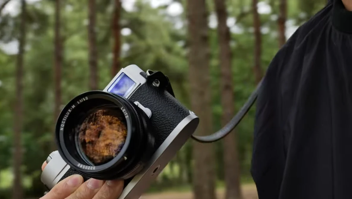 Vintage rangefinder camera with standard lens held in hand outdoors with trees in background.