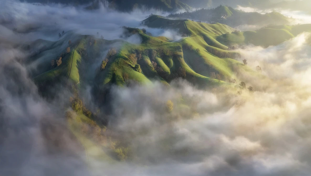 Mountain peaks with verdant slopes emerging from dense clouds and mist under dramatic lighting.