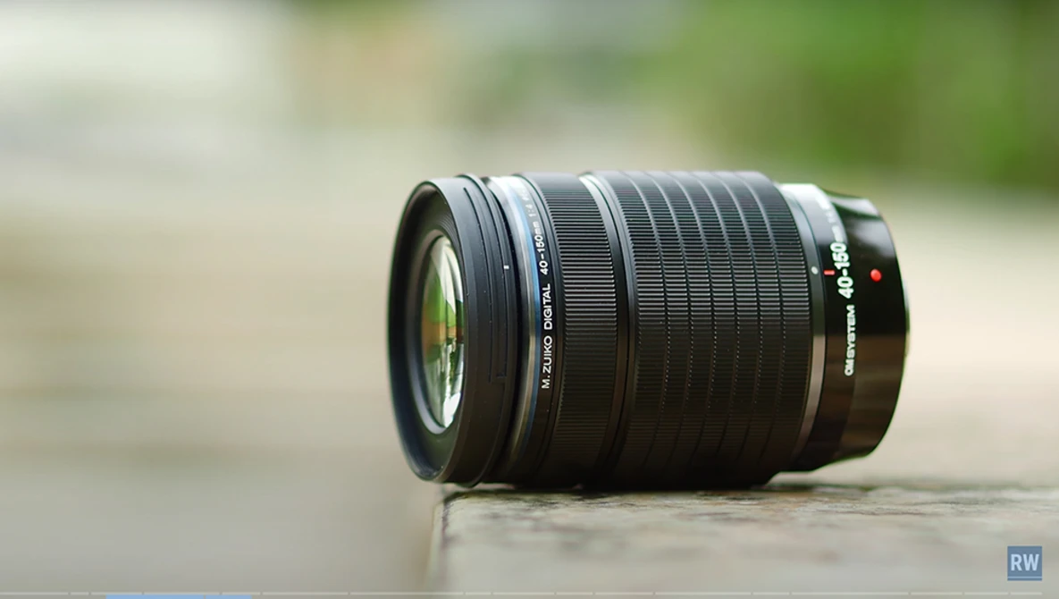 Black telephoto lens with multiple glass elements visible through the barrel, displayed on a neutral surface.