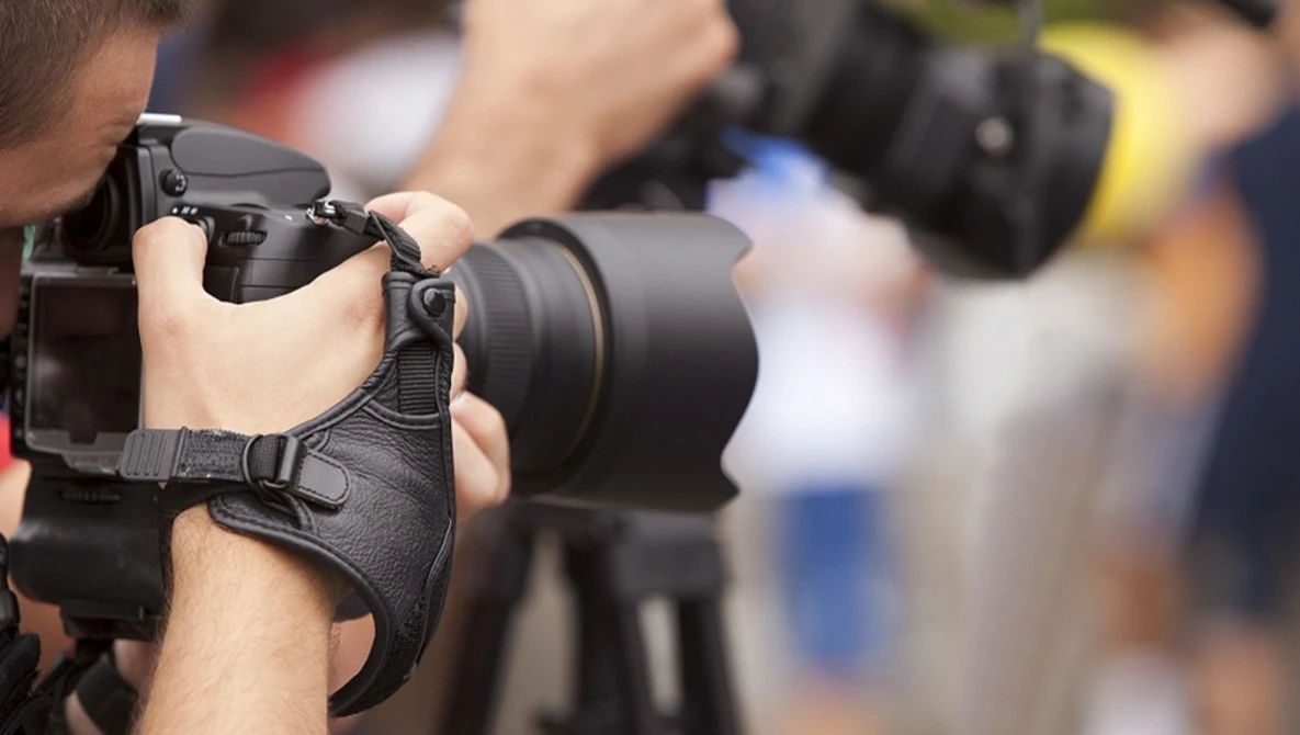 Photographer holding a DSLR camera with telephoto lens at an outdoor event.