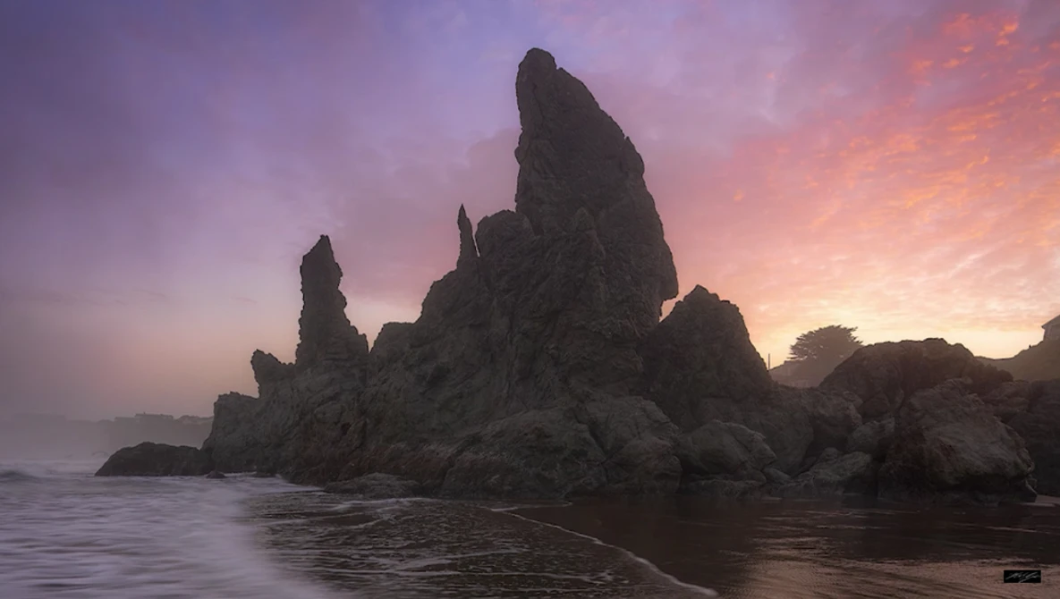 Dramatic rocky sea stacks silhouetted against a purple and pink sunset sky with calm water in foreground.