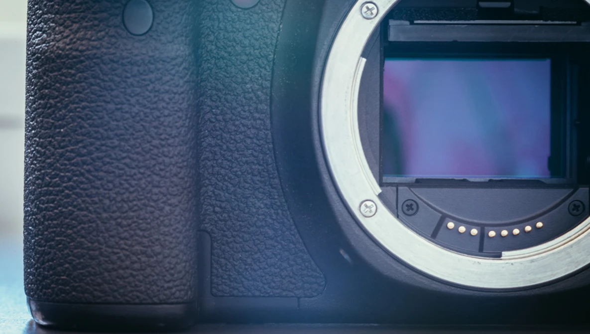 Close-up of a mirrorless camera body showing the textured grip on the left and the open sensor mount with mirror assembly on the right.
