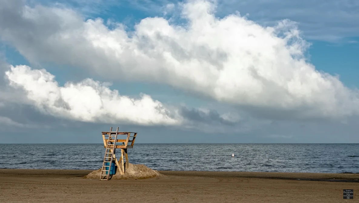 Wooden lifeguard tower on an empty beach under a dramatic cloudy sky.