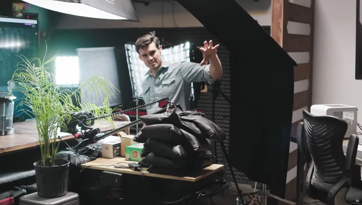 Podcaster gesturing while speaking into a microphone in a home studio setup.
