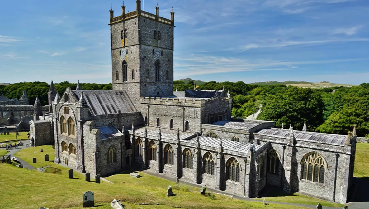 Medieval stone cathedral with square tower surrounded by graveyard, shot under blue sky with green landscape.