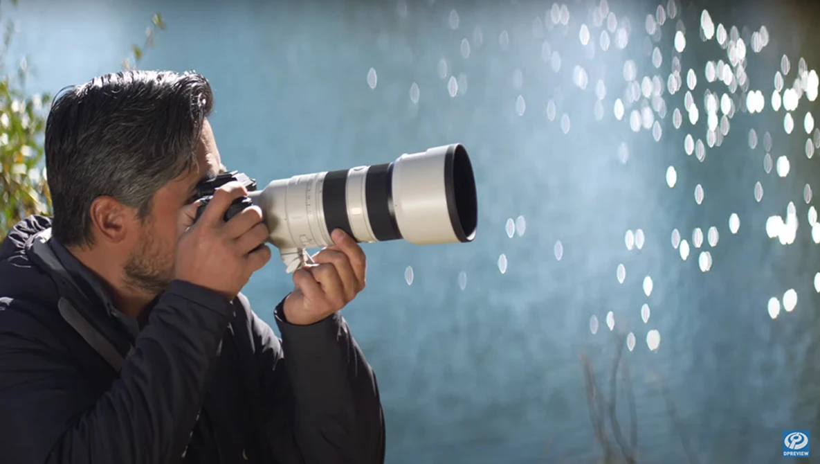 Photographer holding telephoto lens pointed at bokeh lights against blue background.
