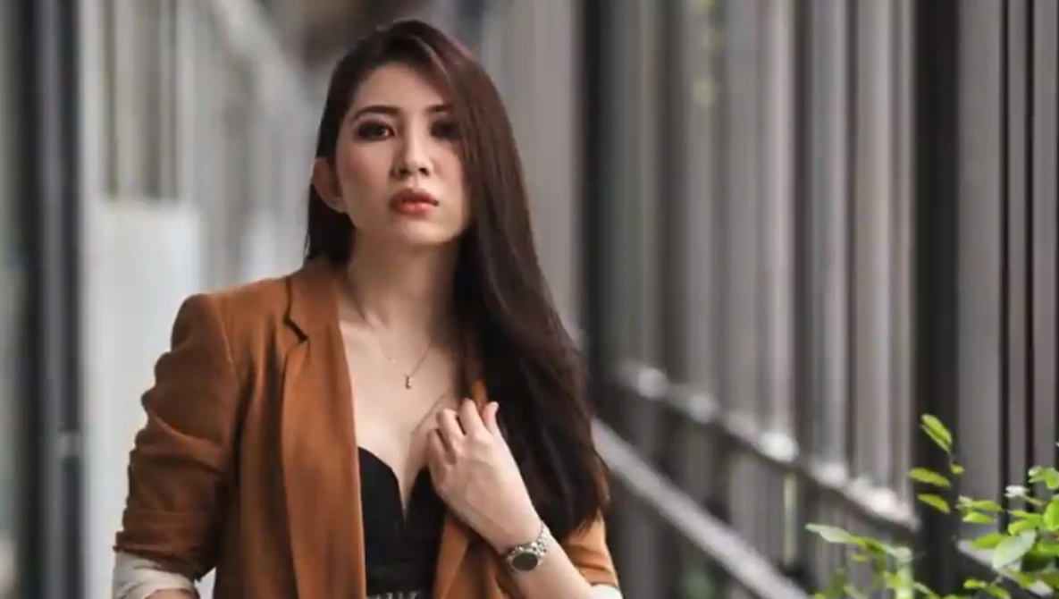 Woman in brown blazer and dark top looking upward in urban corridor setting.