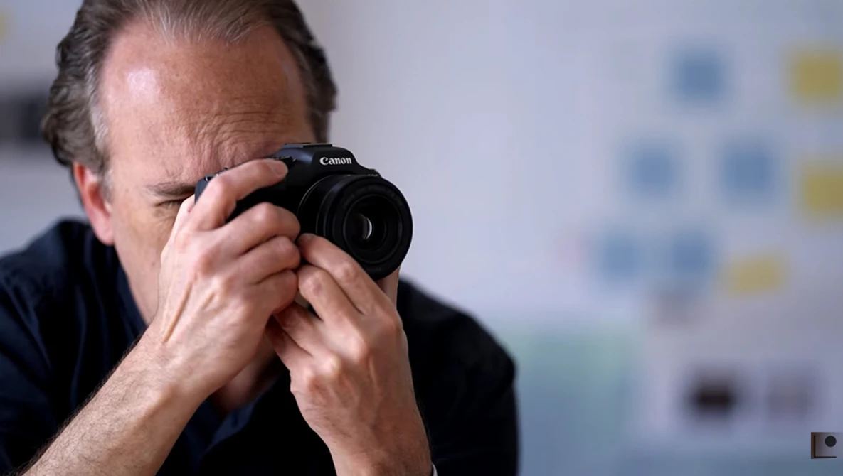 Photographer holding a Canon camera to his eye, composing a shot with focused concentration.