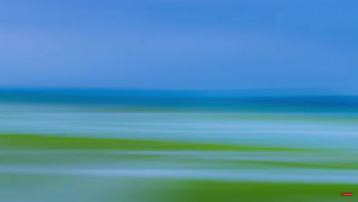 Horizontal bands of blue sky, turquoise water, and green seaweed or algae in calm coastal waters.